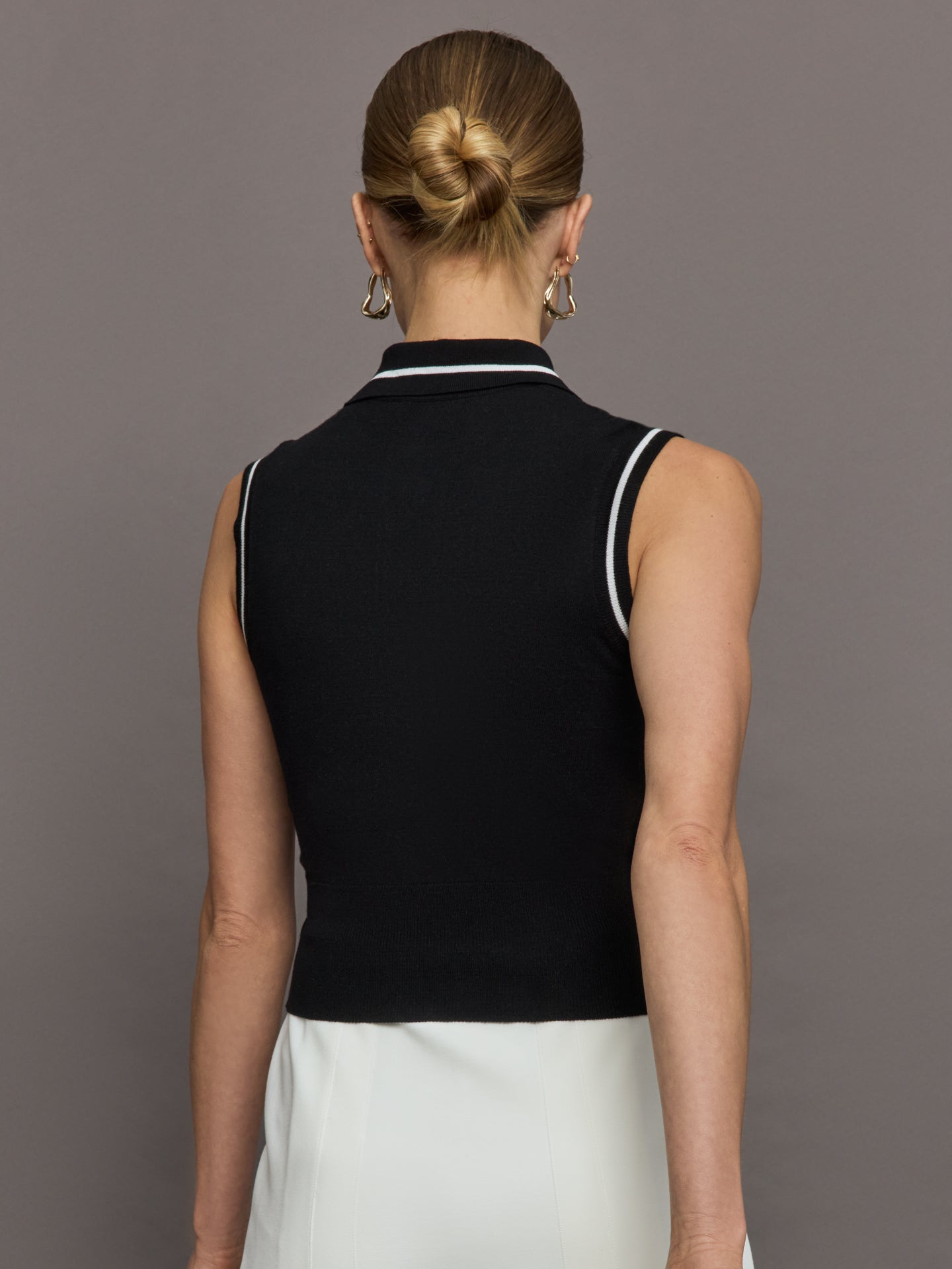 Model wears a sleeveless black tennis polo with three white buttons. 