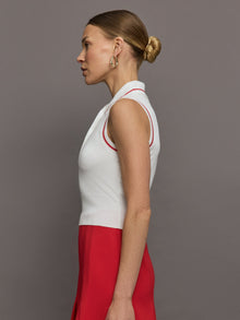 Model wears a sleeveless white tennis polo with three buttons and red seam detailing. 