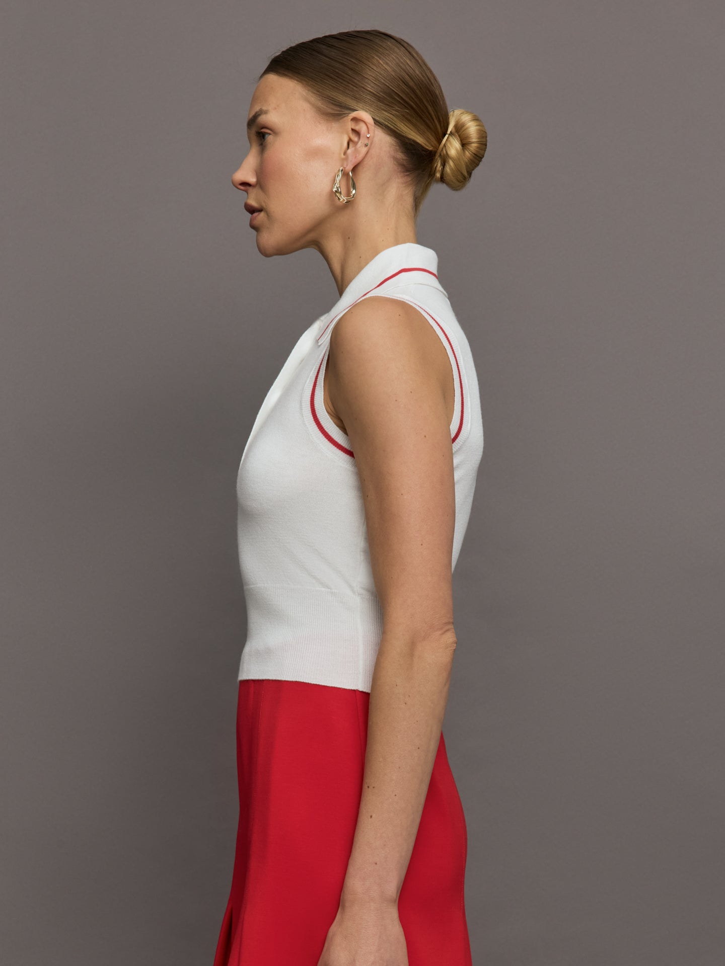 Model wears a sleeveless white tennis polo with three buttons and red seam detailing. 
