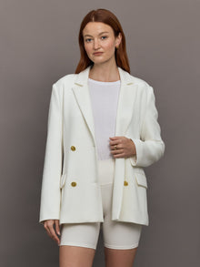 Model wears the white double-breasted blazer in Scuba, with a tailored fit, and a smooth, contoured finish.