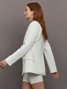 Model wears the white double-breasted blazer in Scuba, with a tailored fit, and a smooth, contoured finish.