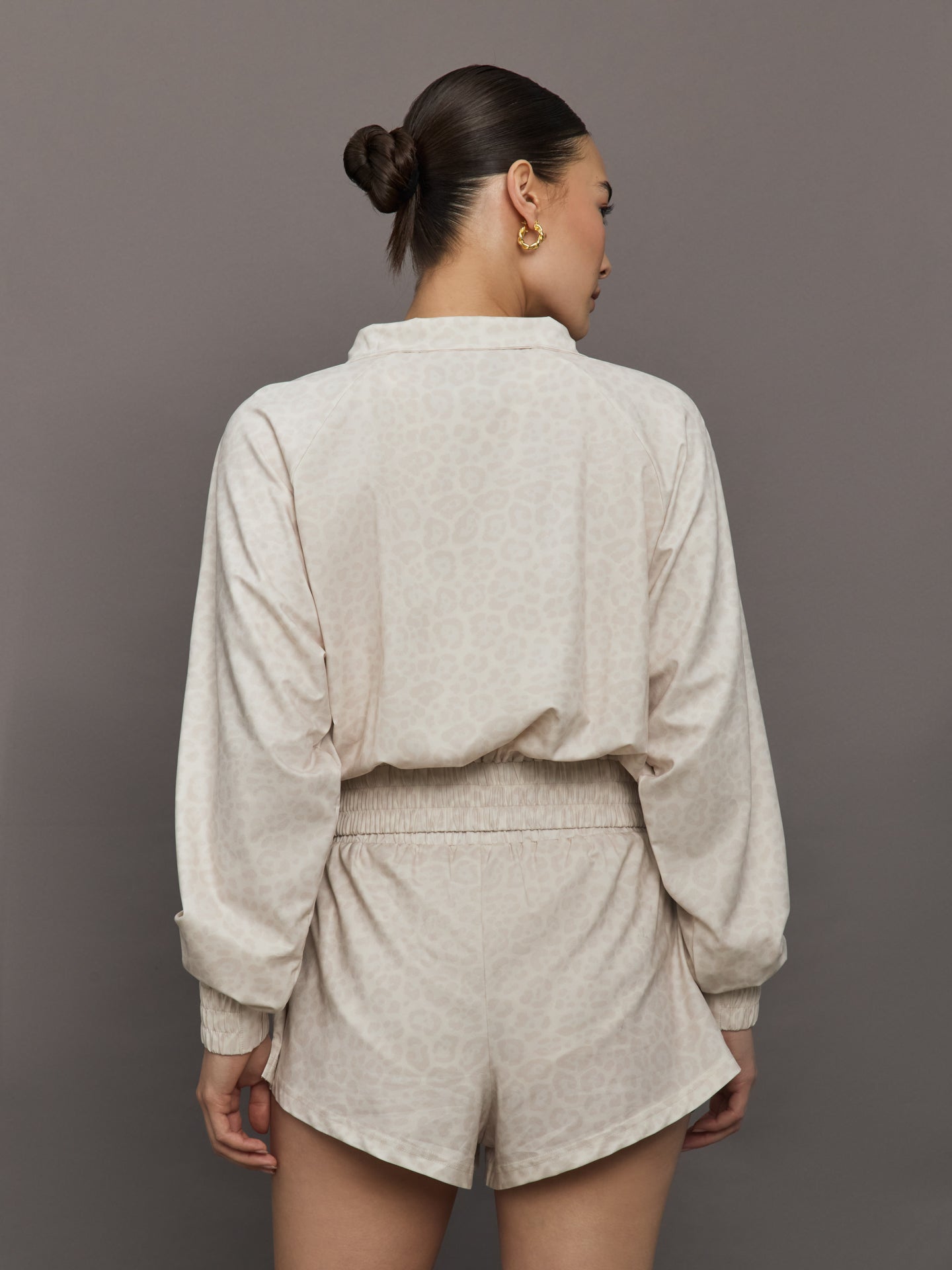 Model wears lightweight windbreaker with a snow leopard print, front zipper, and collared neck.
