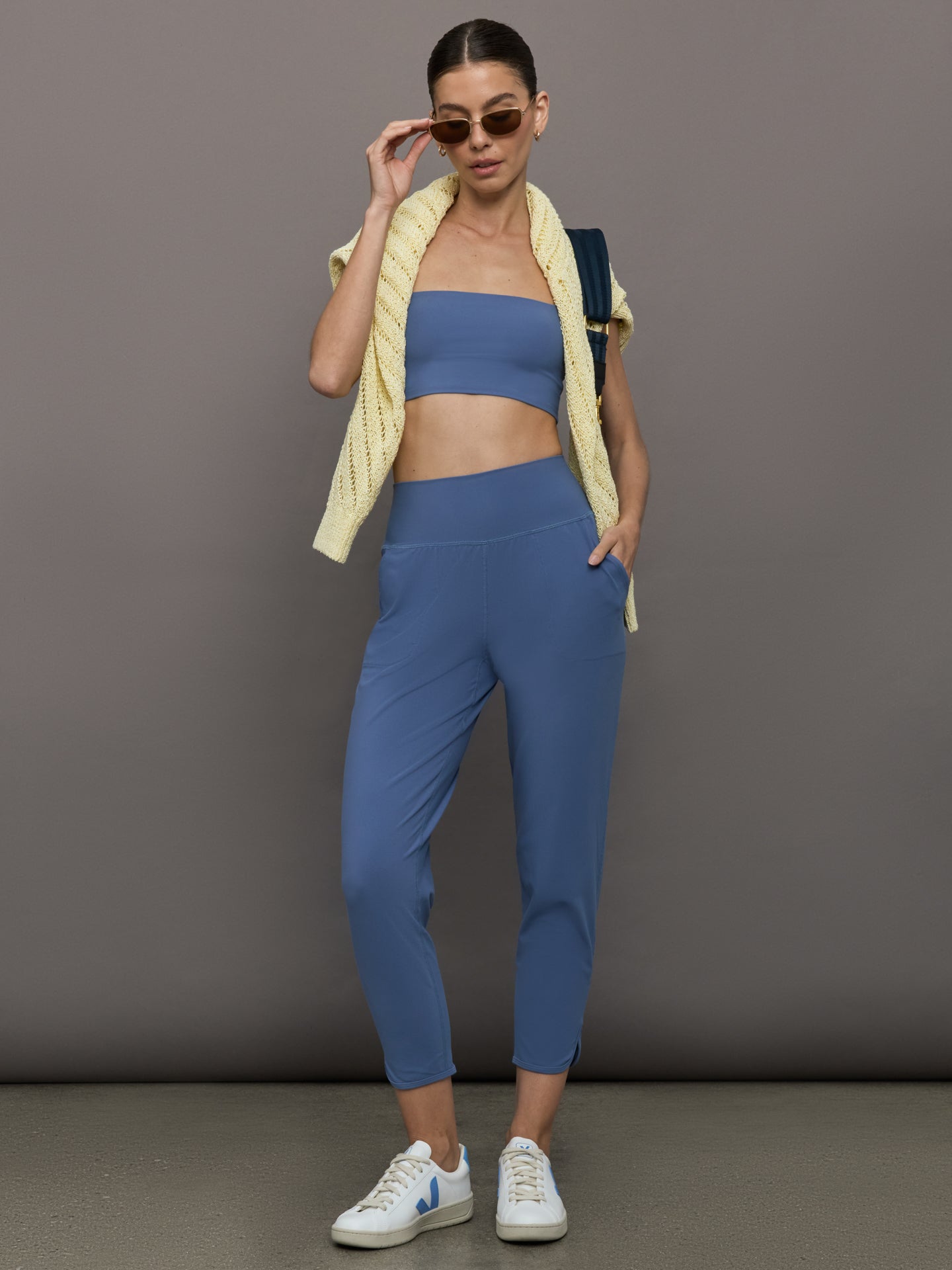 Model wears a pair of lightweight blue joggers with a wide waistband and pockets. 