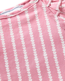 A close-up of pink fabric with vertical rows of small white hearts suggests it is part of the luxurious Girls Twill Amelie Short Set in Love Lines by Petite Plume, featuring a slightly textured material and visible seams indicative of premium sleepwear.