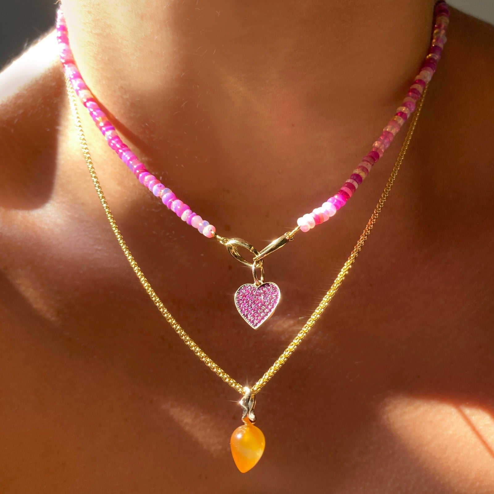 Shimmering Fuchsia Opal Necklace of smooth opals with various shades of pink, styled on a neck with a Ruby Pavé Heart Charm and a gold chain with a carnelian acorn drop charm