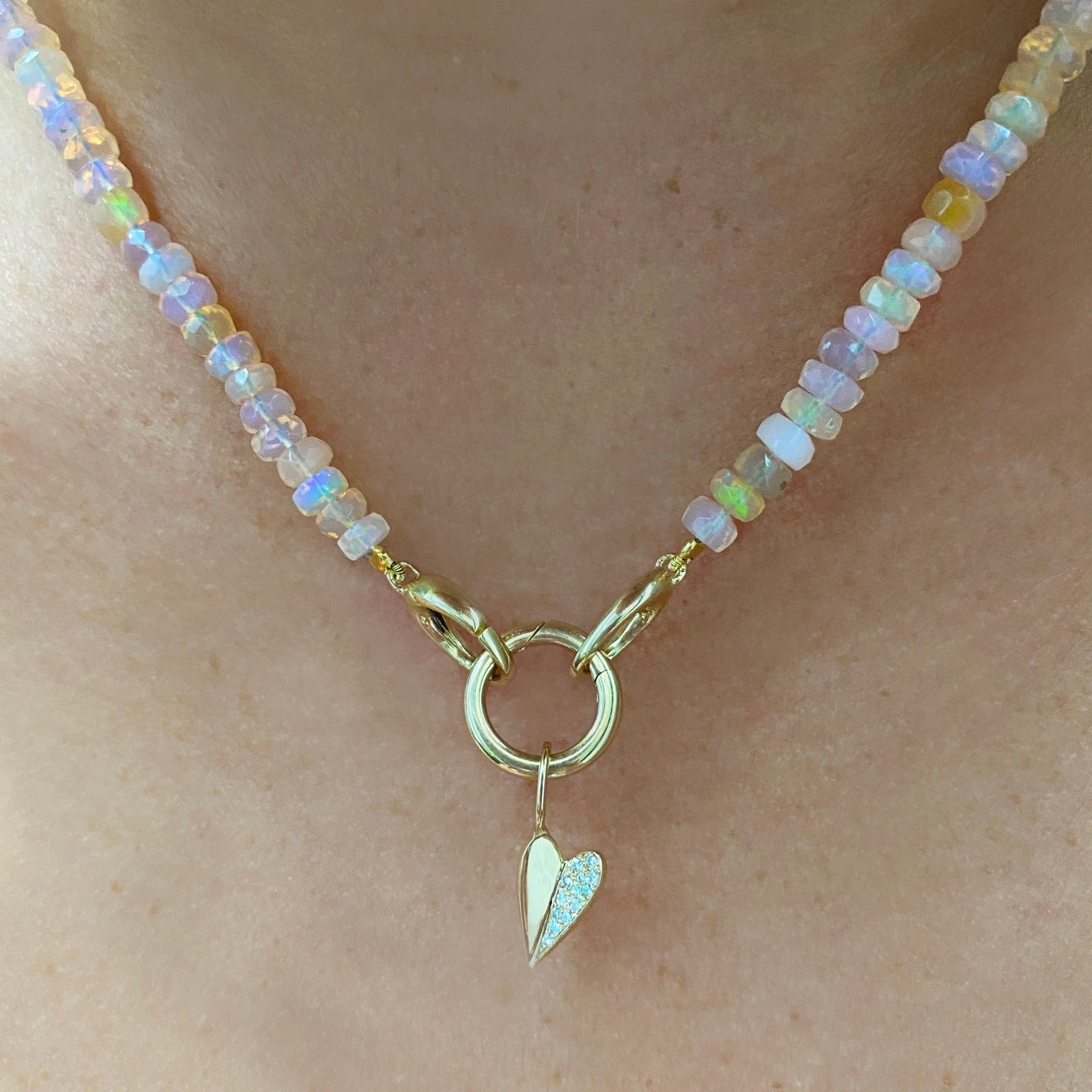 14k yellow gold small folded heart charm with pave diamonds on the right side. Styled on a neck hanging from a rounded charm lock, locked onto oval clasps of a beaded necklace.