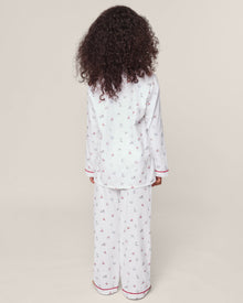 A child with curly hair, wearing a Petite Plume Kids Twill Pajama in Coastal Charms, featuring white yarn-dyed cotton and red and blue patterns, stands with their back to the camera against a plain background.
