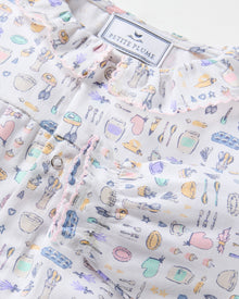 The Baby's Twill Madeline Romper in Baking Spirits Bright features long sleeves, a ruffled collar and cuffs, pastel kitchen print on white, front buttons, and snap closures at the legs for easy dressing.