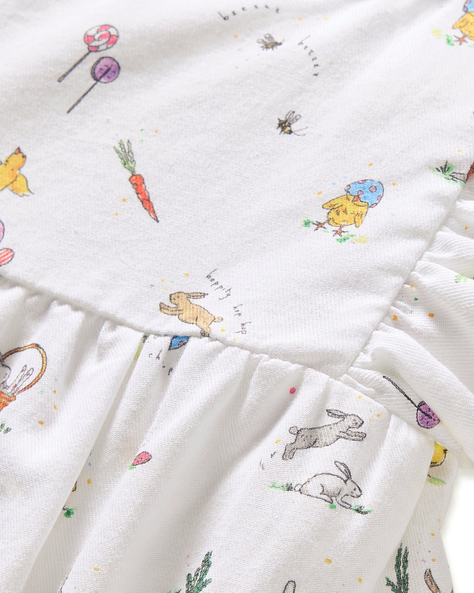 A young child with brown hair in pigtails wears the Baby's Twill Ruffled Romper in Easter Frolic, featuring colorful animal and floral prints, standing against a plain light background.