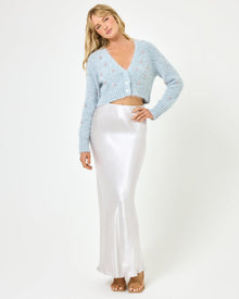 Full-length front view of a model wearing the LSPACE Sweet As Honey Skirt in silver, a high-waisted bias-cut satin maxi skirt with a fluid drape, paired with a pale blue embellished cropped cardigan and flat sandals on a white background.