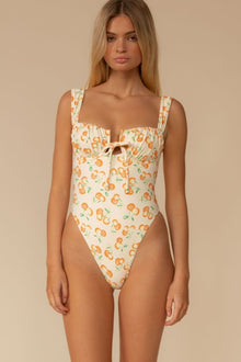 Cream one-piece swimsuit with orange and green cherry print, square neckline, and tie front detail.