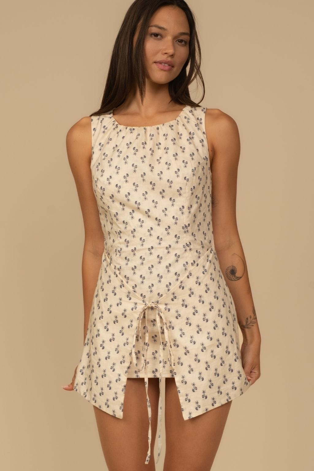 Sleeveless cream dress with small dark floral print and front drawstring tie detail.