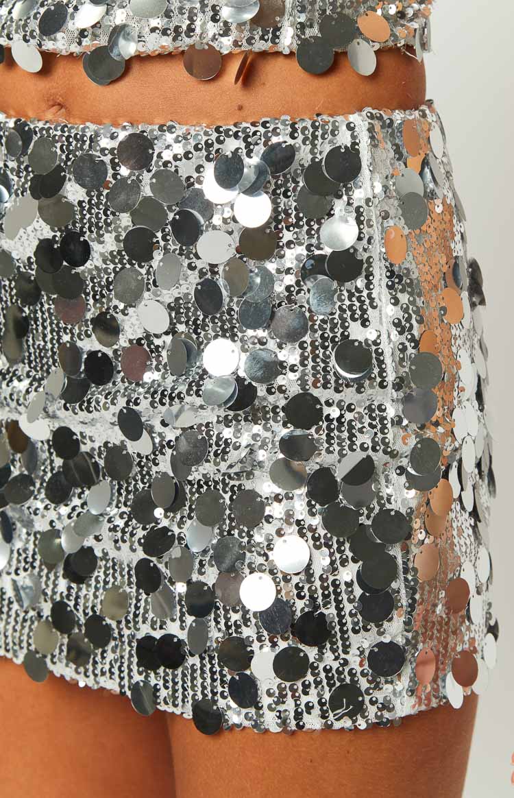Close-up of the silver sequin mini skirt fabric, highlighting the dense shimmering base and larger reflective round sequins