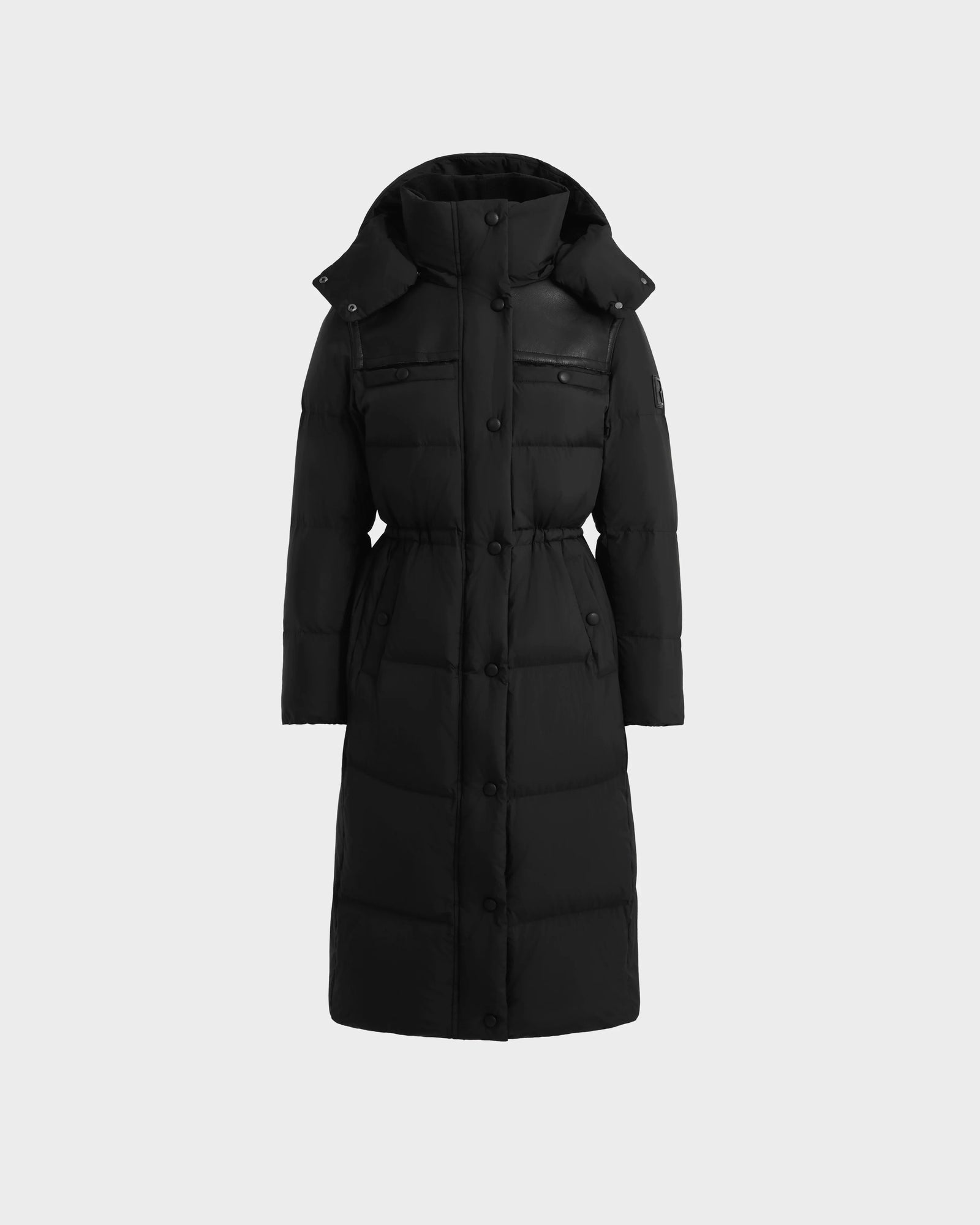 The Rudsak EMBER M-L - L125543 Black is a women’s long down puffer coat with a removable hood, snap buttons, two zippered chest pockets, and a fitted waist—crafted from sleek faux vegan leather on a plain light background.