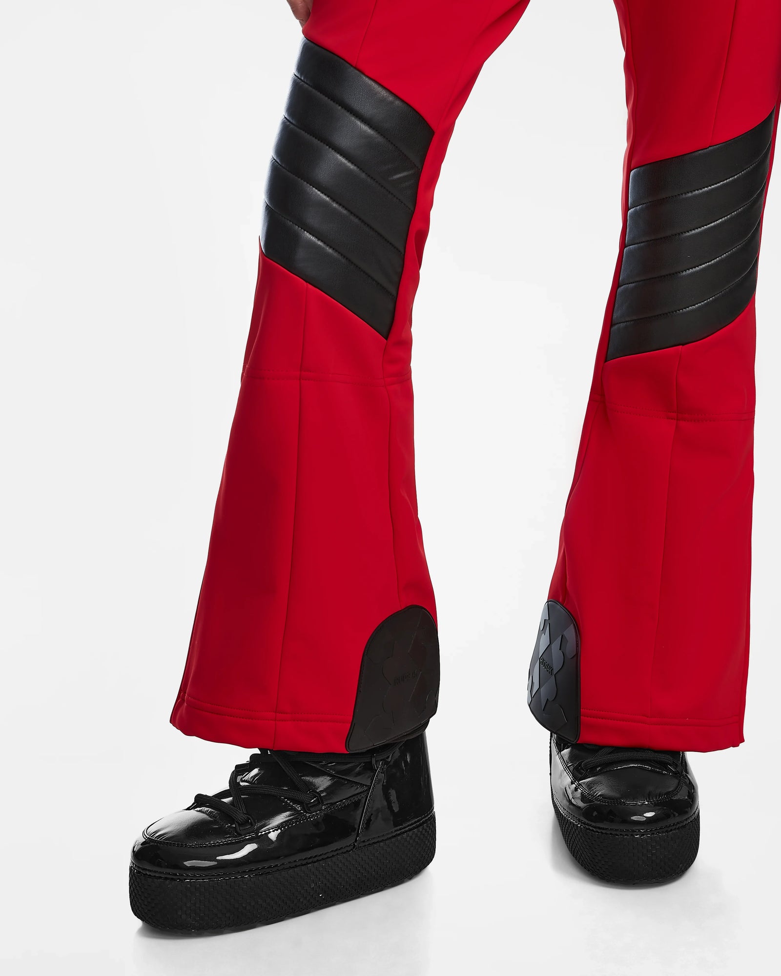 A person models Rudsaks ARLEY - 8124717 Flame Red pants with black padded panels and shiny black platform shoes, standing against a white background with only the legs and feet visible.