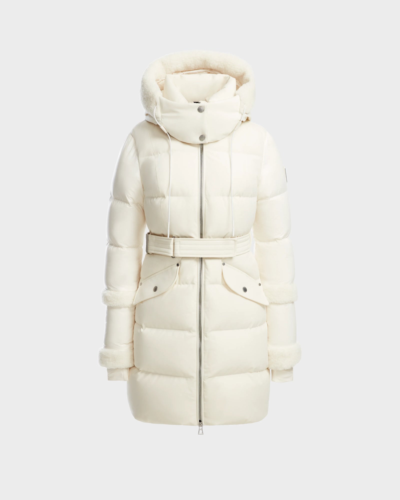 The AUDREY L - 8124585 Iceland by Rudsak is a white, knee-length down puffer jacket featuring a hood with faux fur trim, high collar, belted waist, front zipper, and snap buttons—made from recycled Stormshell fabric for stylish warmth.