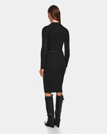 A woman faces away in the CARLI - 8524573 Black fitted knit dress by Rudsak, styled with a vegan leather belt and knee-high black boots. Her straight brown hair cascades down her back against a plain light background.