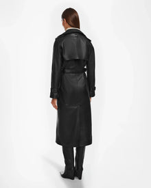 A person with straight brown hair, seen from behind, wears the Rudsak CASSIE L - 8124531 black leather trench coat and knee-high black boots, standing against a plain white background.
