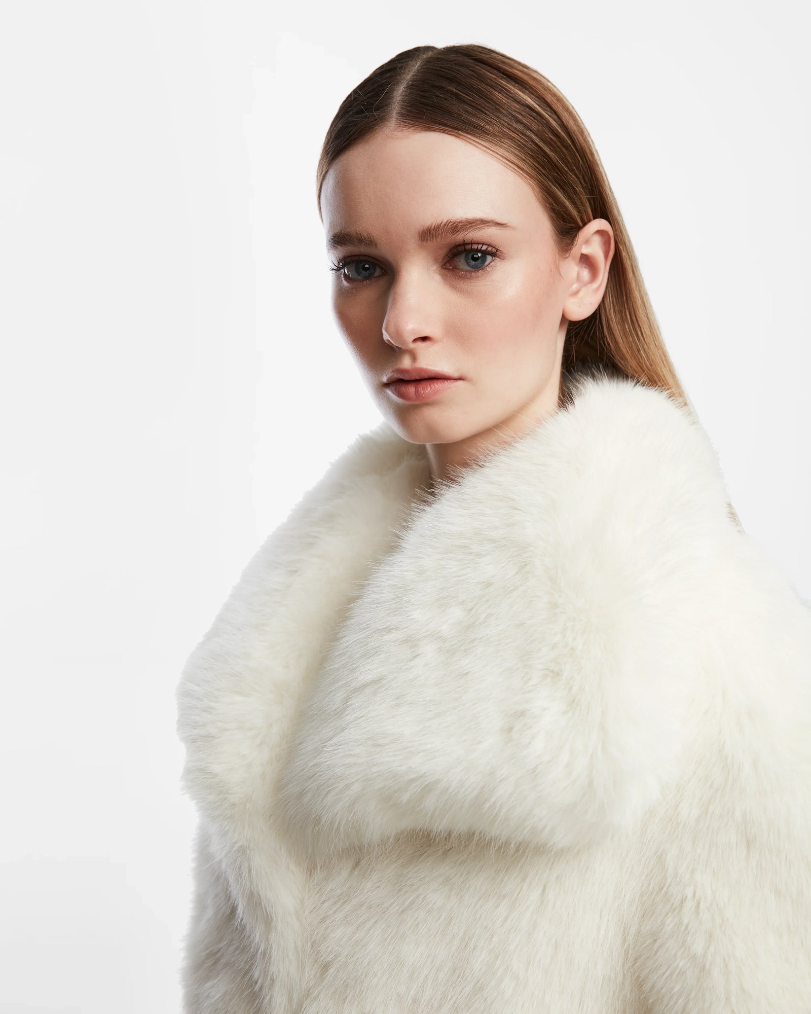 A woman with straight, light brown hair and blue eyes wears the Rudsak CHLOE - L124564 Iceland womens faux fur jacket, looking at the camera against a plain white background—an essential winter wardrobe addition.