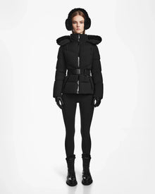A woman faces forward against a white background, wearing the Rudsak CHRISTELLE M - L123525 Black quilted down puffer with a fur-lined hood, matching earmuffs, gloves, leggings, and lace-up boots.