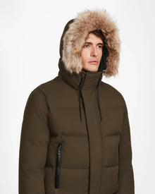 A person wears the Rudsak DALLAS - M122501 Army men's quilted down bomber with a fur-lined hood, facing forward with a neutral expression against a plain white background.