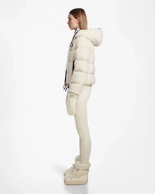 A woman stands in profile against a white background, wearing the DANI S - 8124537 Iceland cream cropped ski jacket by Rudsak, paired with matching mittens, fitted leggings, and fur-trimmed winter boots.