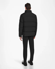 A man faces away, wearing the Rudsak KARLS - M124505 Black men’s puffer jacket with RDS-certified down, paired with black pants and shoes against a plain white background.