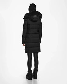 A person stands facing away against a plain white background, wearing the Rudsak KEHLANI - L124540 Black quilted down coat with a fur-lined hood—an essential winter piece combining warmth and style.