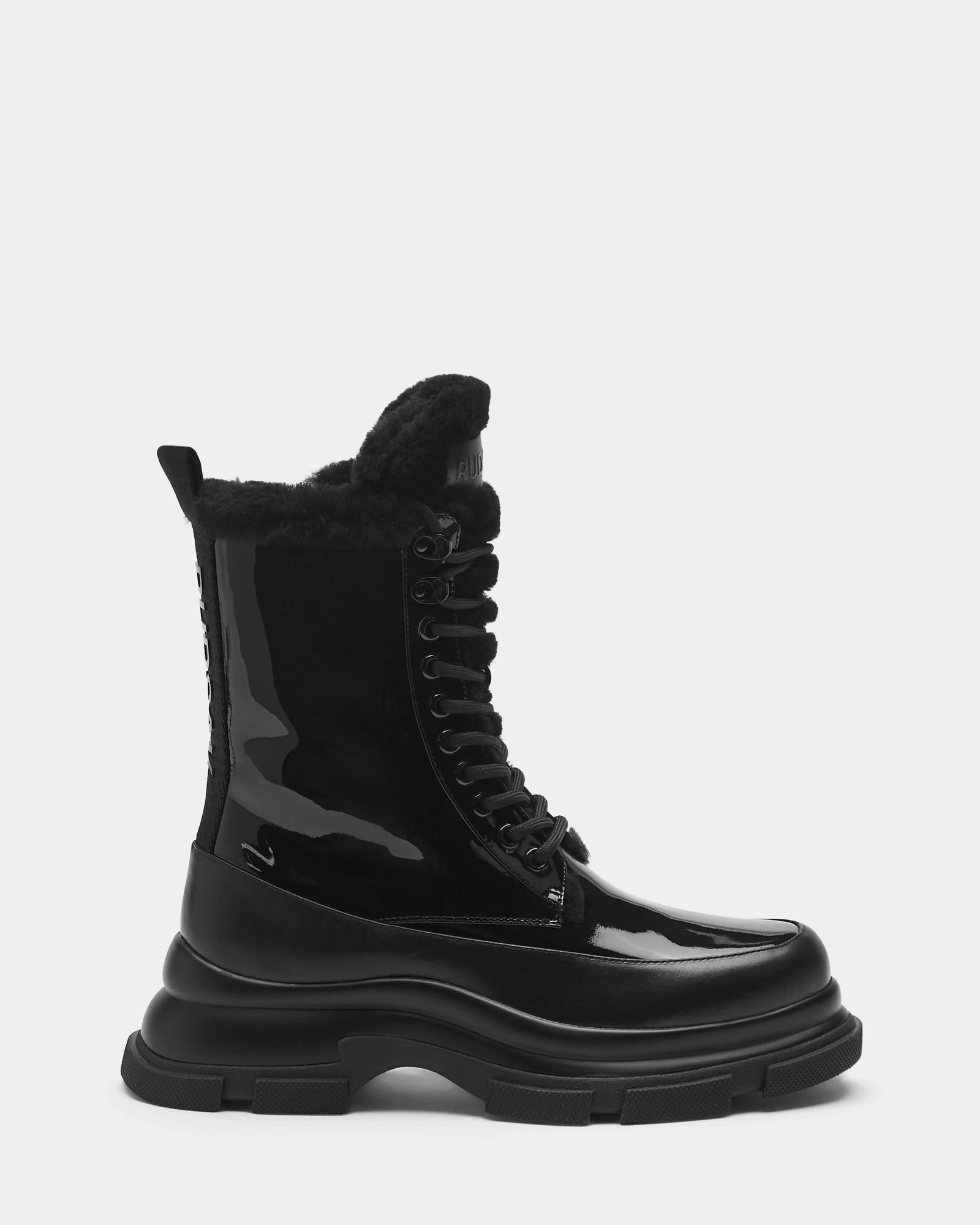The Rudsak LANA - 8223506 BLACK is a shiny black mid-calf lace-up boot with a chunky sole and plush shearling lining, shown in side profile against a plain light background.