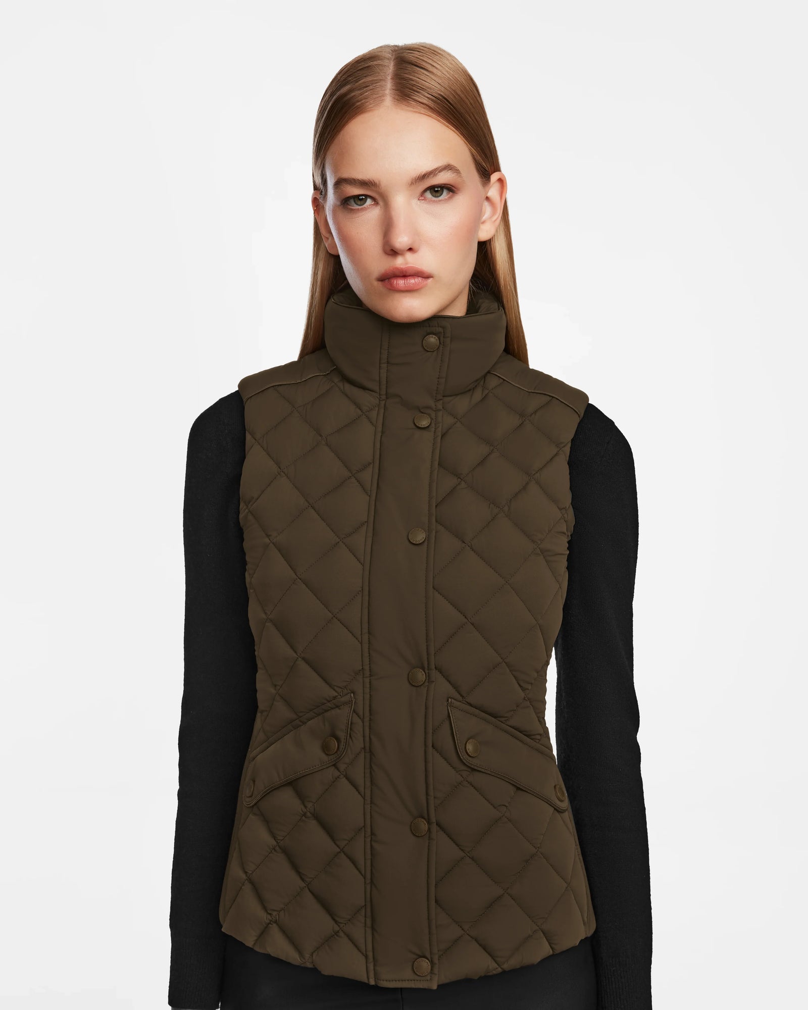 A woman with straight, light brown hair models the Rudsak MATILDA - L124504 Army dark olive womens vest over a black long-sleeve top against a plain white background.