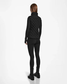 A person faces away, wearing the Rudsak MATILDA - L124504 Black quilted women’s light vest over a black long-sleeve top, leggings, and boots—ideal for transitional weather—against a plain white background.