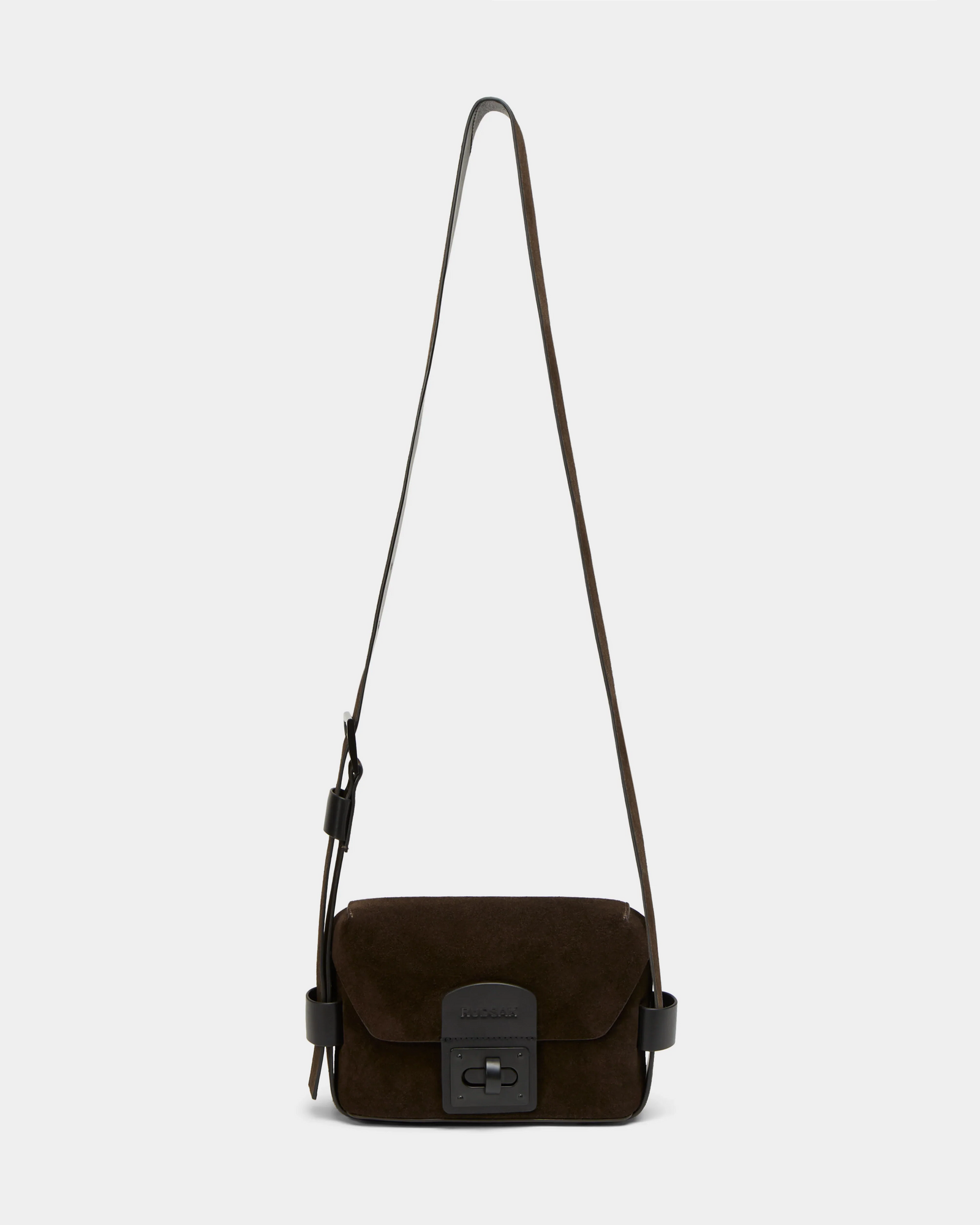 The Rudsak OFILIA S - 8324521 Espresso is a dark brown suede crossbody bag with a long adjustable strap, front flap, and black rectangular clasp, shown against a plain light gray background.
