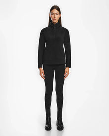 A woman with straight brown hair wears the Rudsak ORCHID - 8524616 Black women’s half-zip pullover with vegan leather trims, black leggings, and ankle boots, standing facing forward against a plain white background.