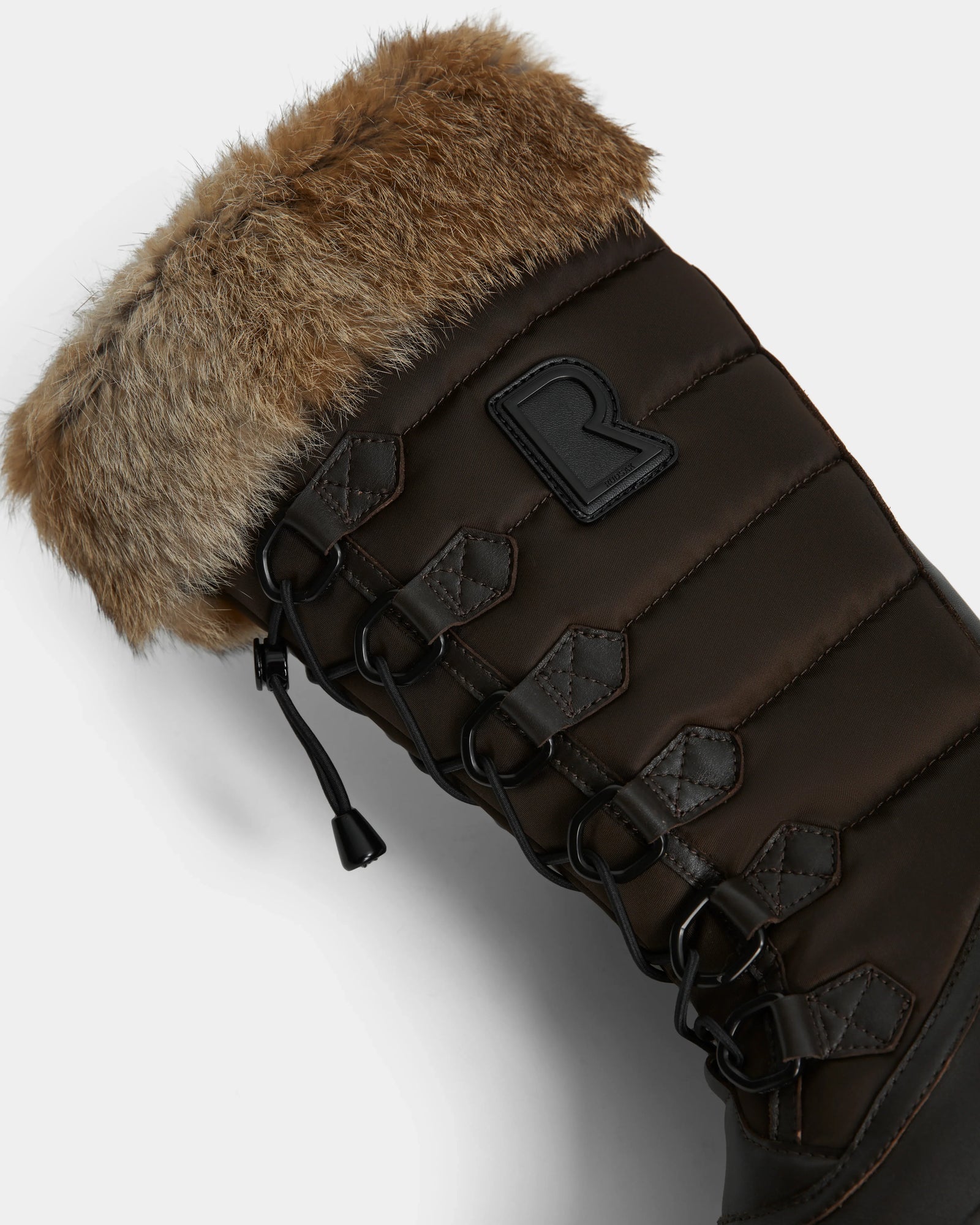 Close-up of Rudsak’s WINDY - L224507 Espresso womens winter boot in dark brown, with black laces, metal eyelets, faux fur trim, and a stitched R logo on the padded side for cozy cold-weather style.