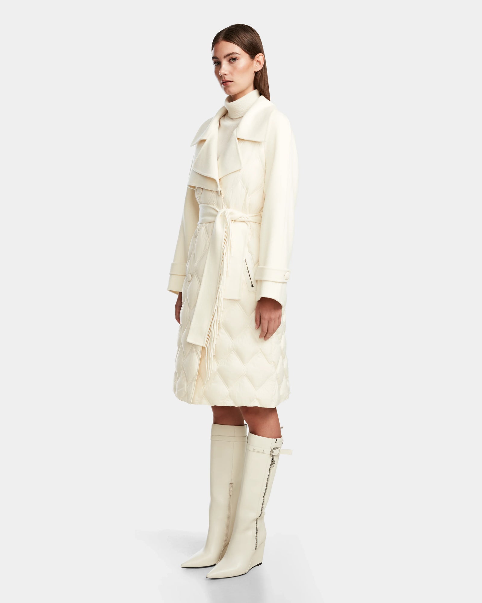 A woman stands in profile wearing the Rudsak ZOE - 8124711 Iceland cream trench coat with quilted detailing, paired with matching knee-high boots against a plain light gray background.