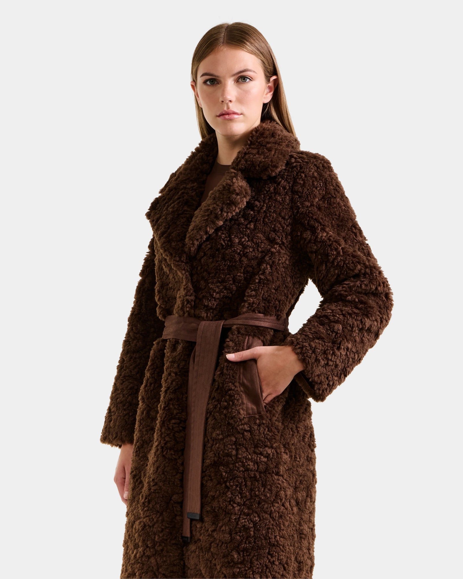 A woman with straight brown hair and a neutral expression models the Rudsak ANNABELLE FSU - L125512 Espresso sherpa teddy coat, featuring a wide collar and matching belt, against a plain light grey background.