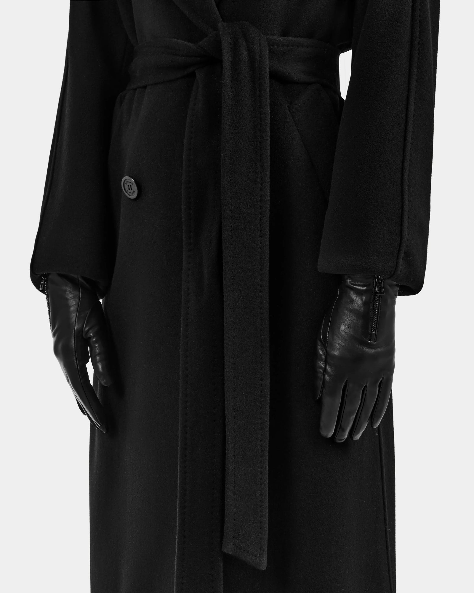A person wearing the Rudsak AUGUSTA - L425546 Black long coat with a fabric belt and women's lamb leather gloves, shown from the shoulders down against a white background—a true cold-weather essential.