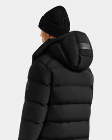 A person faces away, wearing the Rudsak BRAYDEN M-S - M125524 Black down puffer with hood and arm patch, plus a black knit beanie; 