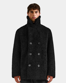 A person wearing the Rudsak ELTON - M125534 Black double-breasted overcoat with a high collar stands against a plain light background, looking straight at the camera.