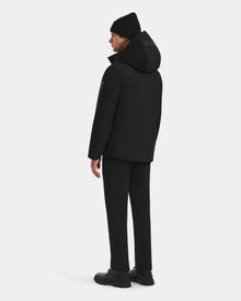 A man faces away, dressed in the Rudsak LAZIO - 6125527 Black down and feather fill men’s parka, with black beanie, pants, and shoes, set against a plain white background.