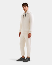 A man with short brown hair wears the Rudsak LEROY - U525509 Vanilla M premium off-white hoodie and matching joggers, paired with black sneakers, standing simply styled against a plain light background.