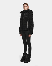 A woman with straight brown hair and a neutral expression stands against a plain background wearing the MIRRY FF - L124507 Black womens short down puffer jacket, paired with black leggings and winter boots.