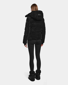 A person stands facing away, wearing the MIRRY FF - L124507 Black velvet corduroy puffer jacket with black leggings and boots against a plain light gray background.