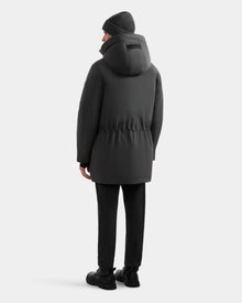 A person in the Rudsak MITCHELL - M125513 Grey men’s down parka stands facing away from the camera, dressed in black pants, black boots, and a gray knit beanie against a plain white background—a true winter essential.
