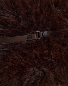 A close-up of the YURI - L425538 Espresso by Rudsak: dark brown fluffy faux fur, brown leather strap, metallic buckle and button fastener—this stylish bucket hat is a perfect winter accessory.