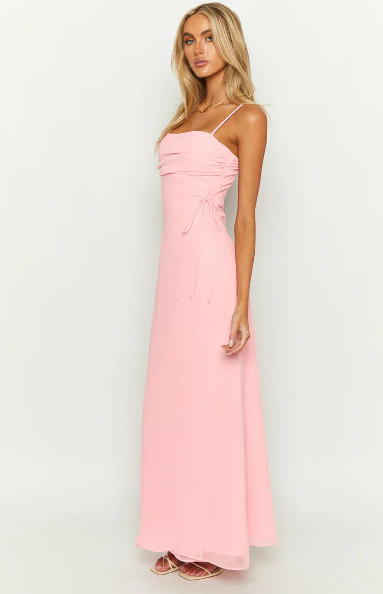 Front view of a pink maxi dress with a straight neckline, ruched bust, thin spaghetti straps, and side tie detail