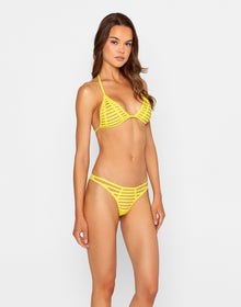 Woman wearing the 'Raja Skimpy Bottom - Sunshine' bikini, a vibrant yellow mesh-strapped bottom with bold cutouts, paired with a matching triangle top. She poses confidently in the back of a car, accessorized with orange sunglasses and gold jewelry under the sun.