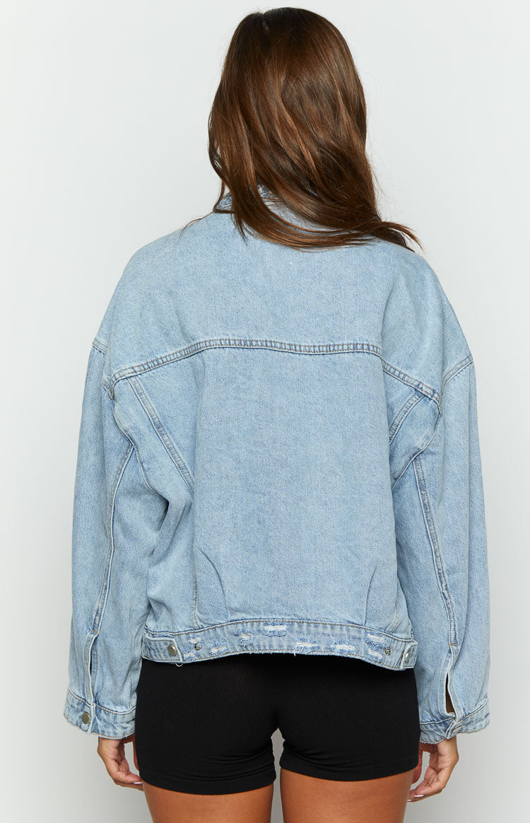 Rear view of an oversized light wash denim jacket with prominent stitching details and a distressed hem