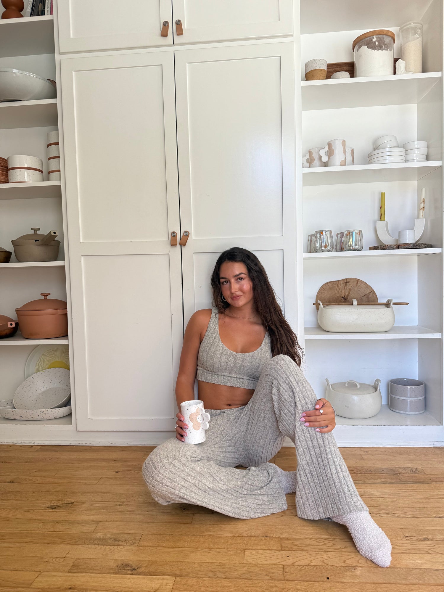 Woman wearing a beige ribbed knit loungewear set, featuring a cropped tank top with a scoop neckline and wide-leg drawstring pants with side pockets, standing barefoot against a plain white background.