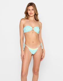 Model modeling the 'Limoncello Spritz Bandeau - Limoncello' bikini top with a center ring detail and gold charm accent, paired with matching tie-side bottoms in a blue gingham print with lemon motifs. Set against a clean, white studio background.